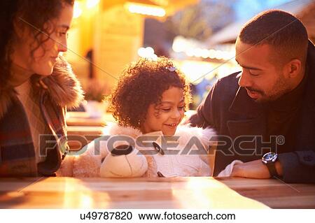 Girl at amusement park holding teddy bear sitting at table with parents View Large Photo Image Stock Image - Girl at amusement park holding teddy bear sitting at table with parents. Fotosearch