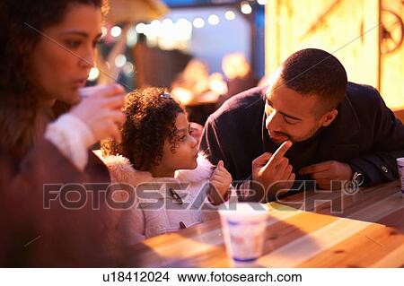 Picture - Girl at amusement park sitting at table with father talking. Fotosearch
