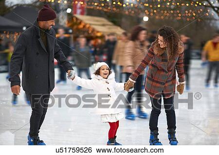 Stock Photograph - Girl holding parents hands ice skating, smiling. Fotosearch