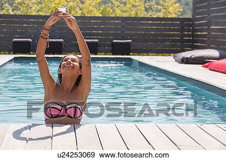 Stock Photo - Girl holding up smartphone for selfie in swimming pool, Cassis, Provence, France. Fotosearch
