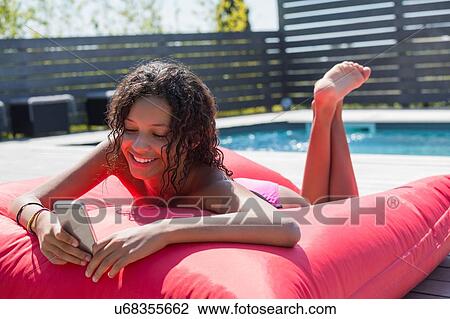 Girl lying on poolside cushion reading smartphone texts, Cassis, Provence, France View Large Photo Image Stock Image - Girl lying on poolside cushion reading smartphone texts, Cassis, Provence, France. Fotosearch