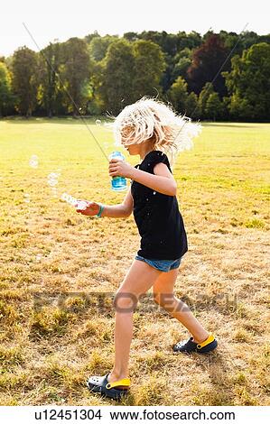 Girl waving bubble wand and making bubbles in park View Large Photo Image Picture - Girl waving bubble wand and making bubbles in park. Fotosearch