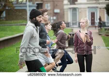 Stock Photo - Group of adults exercising outdoors, young woman holding stopwatch. Fotosearch