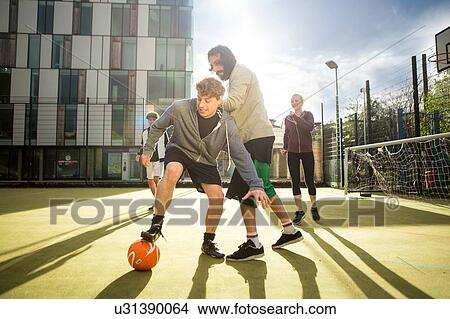 Picture - Group of adults playing football on urban football pitch. Fotosearch