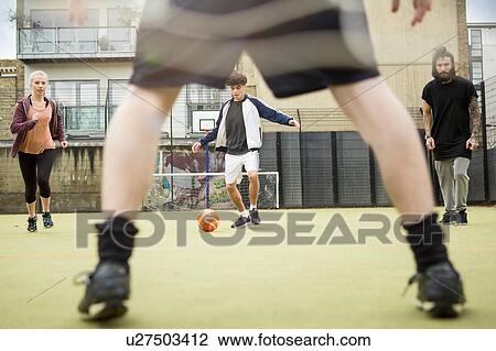 Stock Image - Group of adults playing football on urban football pitch. Fotosearch
