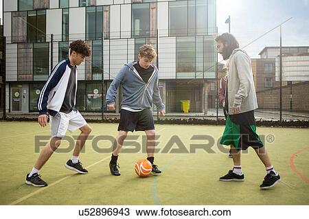 Stock Image - Group of adults playing football on urban football pitch. Fotosearch
