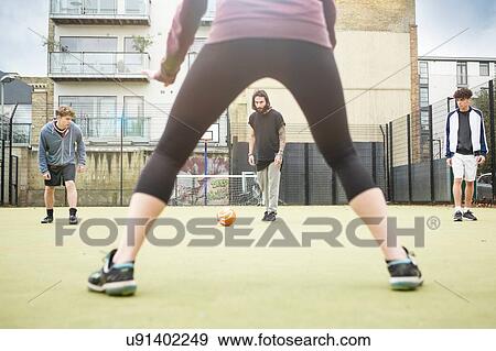Stock Photo - Group of adults playing football on urban football pitch. Fotosearch