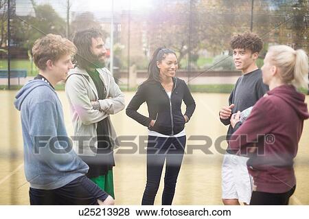 Stock Photo - Group of adults standing on urban sports pitch, talking. Fotosearch