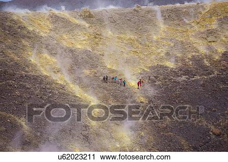 Stock Image - Group of tourists walking through fumarole smoke at Gran Cratere, Vulcano Island, Aeolian Islands, Sicily, Italy. Fotosearch