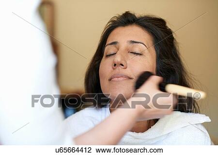 Stock Image - Hands of female make up artist applying blusher to clients cheek. Fotosearch