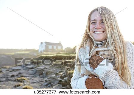 Stock Photo - Happy young woman wrapping up in scarf at beach, Constantine Bay, Cornwall, UK. Fotosearch