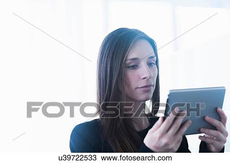 Stock Image - Head and shoulders of young woman using digital tablet. Fotosearch
