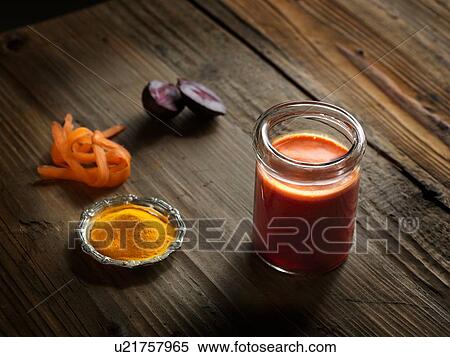 Stock Photography - High angle view of orange raw juice in a jar with beetroot, turmeric and grated carrot on wood grain pattern background. Fotosearch