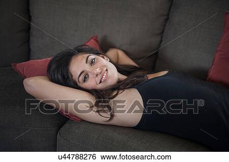 High angle view of young woman lying on back on sofa, hands behind head, looking at camera smiling View Large Photo Image Stock Photograph - High angle view of young woman lying on back on sofa, hands behind head, looking at camera smiling. Fotosearch