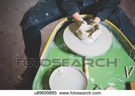 Stock Photography - High angle view of young woman, waist down, sitting at pottery wheel making clay pot. Fotosearch