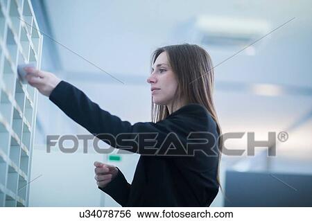 Low angle side view of young woman in office inserting paperwork into pigeon hole View Large Photo Image Stock Photograph - Low angle side view of young woman in office inserting paperwork into pigeon hole. Fotosearch