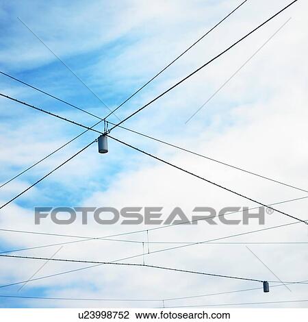 Stock Image - Low angle view of blue sky and street lights with criss crossed wires. Fotosearch