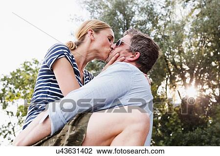 Stock Image - Low angle view of couple sharing passionate kiss in park. Fotosearch