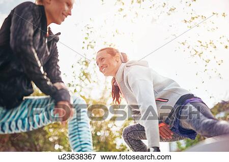 Low angle view of female runners stretching legs in park View Large Photo Image Stock Photo - Low angle view of female runners stretching legs in park. Fotosearch