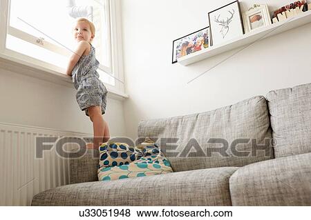 Low angle view of female toddler standing on sofa by window View Large Photo Image Stock Photo - Low angle view of female toddler standing on sofa by window. Fotosearch