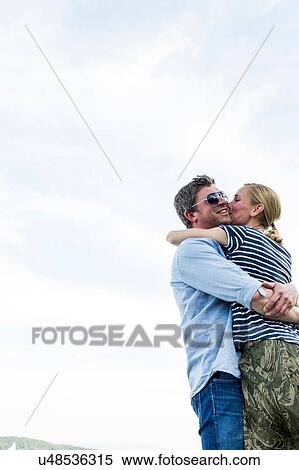 Stock Photography - Low angle view of romantic couple hugging and kissing against sky. Fotosearch