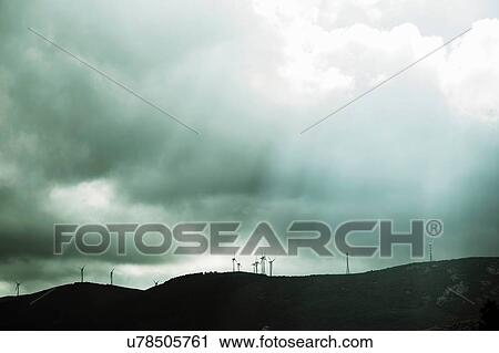 Stock Image - Low angle view of wind farm underneath dramatic stormy sky, Costa Smeralda, Sardinia, Italy. Fotosearch