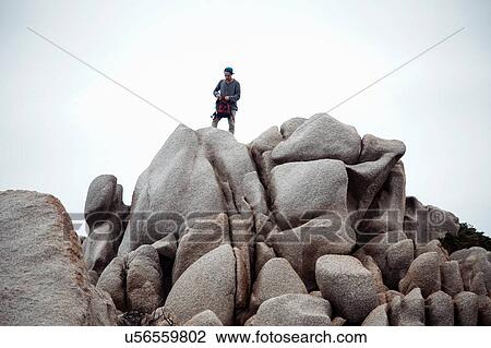 Low angle view of young man standing on rocks holding backpack looking down, Costa Smeralda, Sardinia, Italy View Large Photo Image Stock Image - Low angle view of young man standing on rocks holding backpack looking down, Costa Smeralda, Sardinia, Italy. Fotosearch