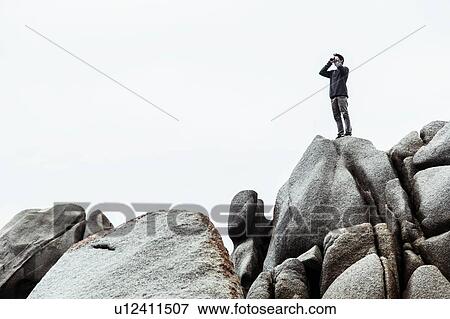 Low angle view of young man standing on rocks, pretending to use binoculars, Costa Smeralda, Sardinia, Italy View Large Photo Image Stock Photo - Low angle view of young man standing on rocks, pretending to use binoculars, Costa Smeralda, Sardinia, Italy. Fotosearch
