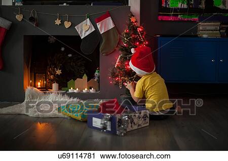 Stock Image - Male toddler preparing christmas tree in front of fireplace. Fotosearch