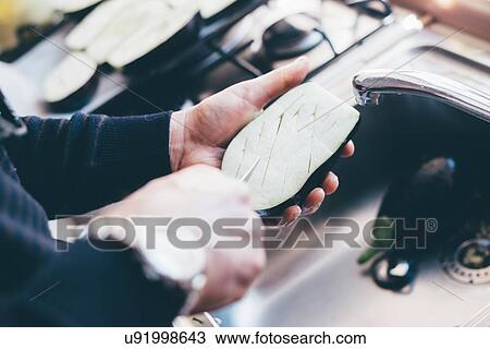 Stock Image - Mans hands making cuts on aubergine halves in kitchen. Fotosearch
