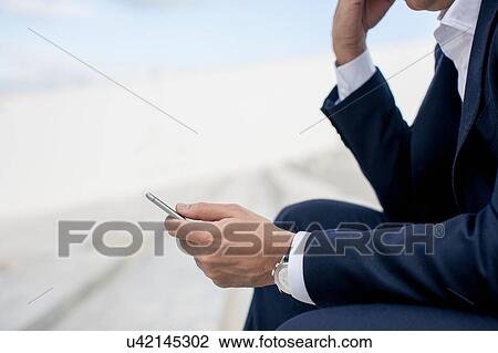Mature businessman sitting outdoors, using smartphone, mid section View Large Photo Image Stock Image - Mature businessman sitting outdoors, using smartphone, mid section. Fotosearch
