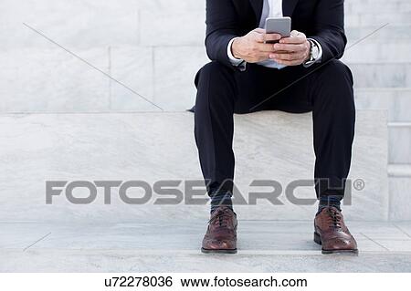 Mature businessman sitting outdoors, using smartphone, low section View Large Photo Image Stock Photograph - Mature businessman sitting outdoors, using smartphone, low section. Fotosearch