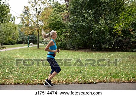 Picture - Mature female runner running in park. Fotosearch