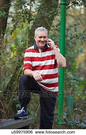 Stock Photograph - Mature male runner chatting on smartphone in forest. Fotosearch