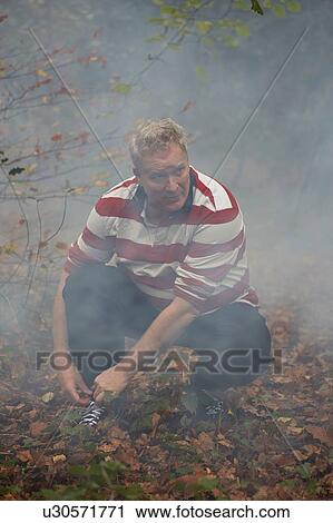 Stock Image - Mature male runner crouching to tie trainer laces in misty forest. Fotosearch