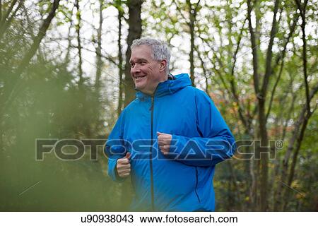 Stock Image - Mature male runner running in forest. Fotosearch