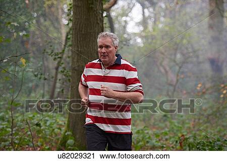 Stock Image - Mature male runner running through misty forest in morning. Fotosearch