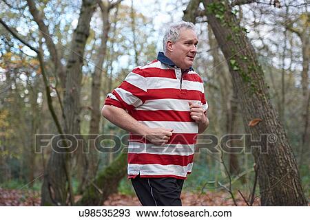 Stock Image - Mature male runner running through forest. Fotosearch