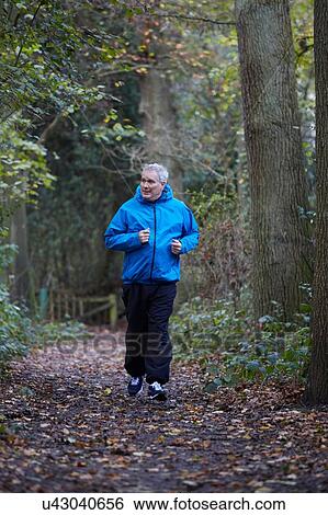 Stock Photograph - Mature male runner running through along forest track. Fotosearch