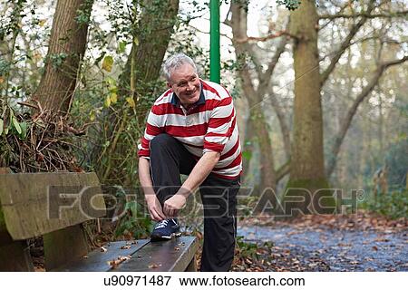 Stock Photo - Mature male runner tying trainer laces on forest bench. Fotosearch