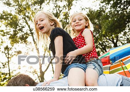 Mature man giving two young daughters piggy back in park View Large Photo Image Stock Photo - Mature man giving two young daughters piggy back in park. Fotosearch