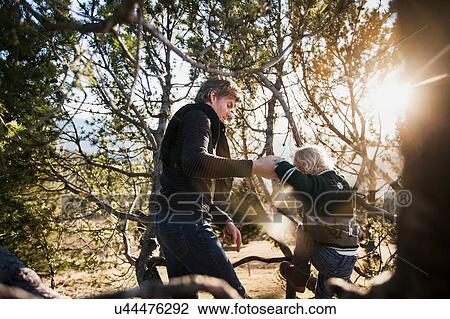 Stock Image - Mature man helping toddler daughter to climb forest tree. Fotosearch