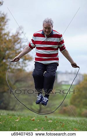 Stock Image - Mature man training in field with skipping rope. Fotosearch