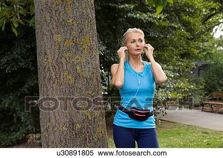 Mature woman adjusting earphones whilst training in park View Large Photo Image Stock Photography - Mature woman adjusting earphones whilst training in park. Fotosearch