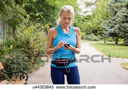 Mature woman choosing smartphone music whilst training in park View Large Photo Image Stock Photography - Mature woman choosing smartphone music whilst training in park. Fotosearch