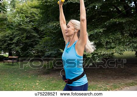 Mature woman lifting hand weights whilst training in park View Large Photo Image Stock Image - Mature woman lifting hand weights whilst training in park. Fotosearch