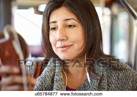 Mature woman on bus journey, wearing earphones, looking at smartphone View Large Photo Image Stock Photo - Mature woman on bus journey, wearing earphones, looking at smartphone. Fotosearch