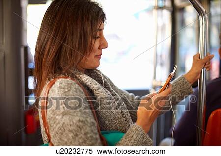 Mature woman on bus journey, wearing earphones, looking at smartphone View Large Photo Image Stock Photography - Mature woman on bus journey, wearing earphones, looking at smartphone. Fotosearch