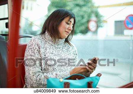 Stock Photo - Mature woman sitting on bus, looking at smartphone. Fotosearch