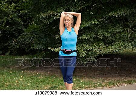 Stock Photo - Mature woman stretching arms whilst training in park. Fotosearch